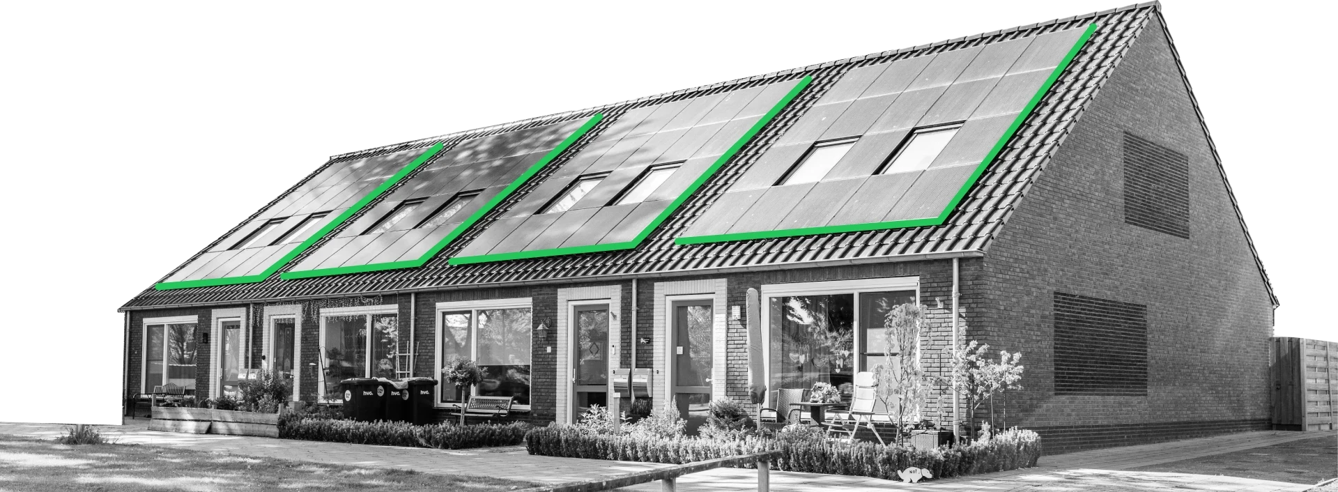 A row of modern brick townhouses with large solar roof panels, surrounded by greenery and trees under a clear blue sky. A wooden fence and paved sidewalk are in the foreground.